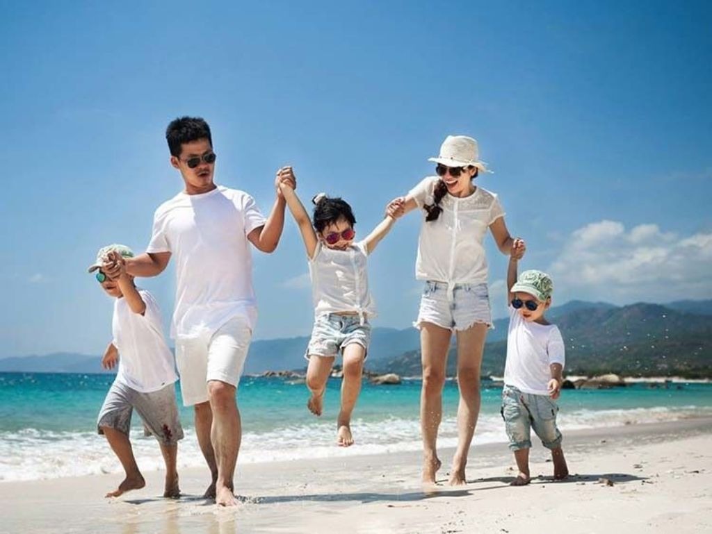 Bố mẹ nắm tay con đi dạo trên bãi biển nắng